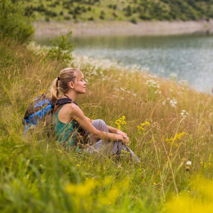 woman sitting in grassy field by lake