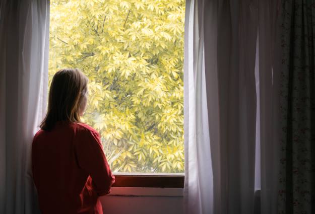 woman in dark room sadly looking out window