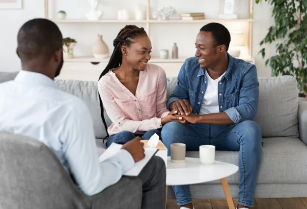 Smiling couple holding hands during a session with their marriage counselor