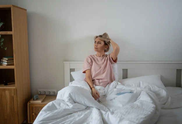 Tired woman sitting up in bed in the morning with low energy